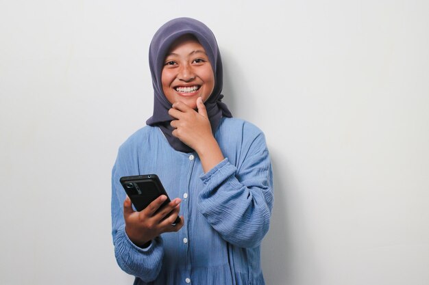 Bella giovane ragazza asiatica in hijab sorridente mentre si tiene lo smartphone