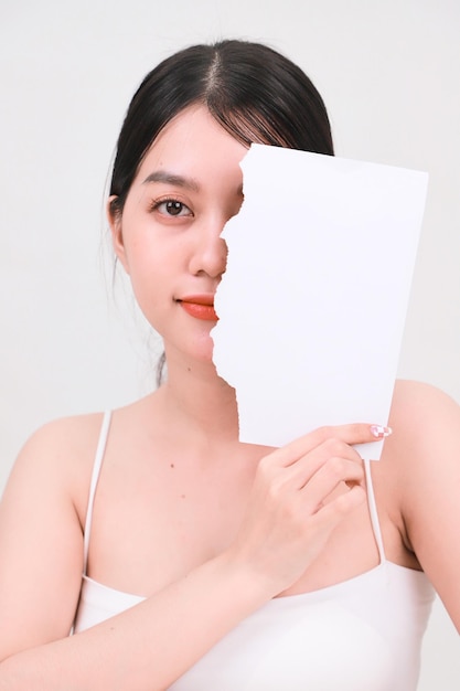 Bella giovane ragazza asiatica in un reggiseno bianco con pelle luminosa e fresca che tiene un pezzo di carta