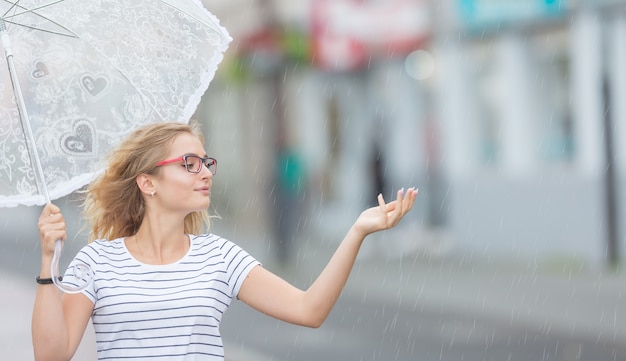 Bella giovane ragazza bionda che tiene ombrello sotto la pioggia estiva.