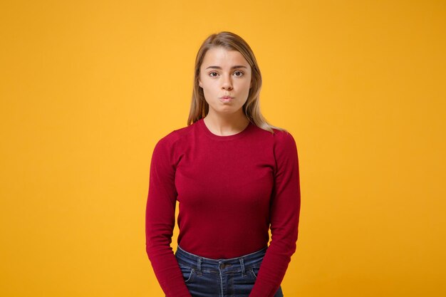 Bella giovane ragazza bionda della donna nella posa degli abiti casual isolata sul ritratto dello studio del fondo della parete giallo arancione. Concetto di stile di vita di emozioni sincere della gente. Simula lo spazio della copia. Labbra che soffiano.