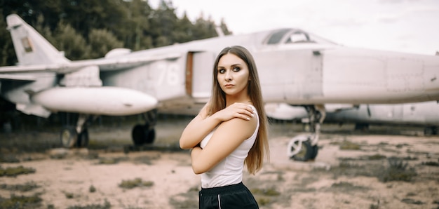 Bella giovane ragazza bruna si leva in piedi sullo sfondo di vecchi aerei militari.