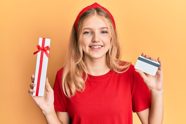 Bella giovane ragazza caucasica che tiene regalo e carta di credito sorridente con un sorriso felice e fresco sul viso che mostra i denti