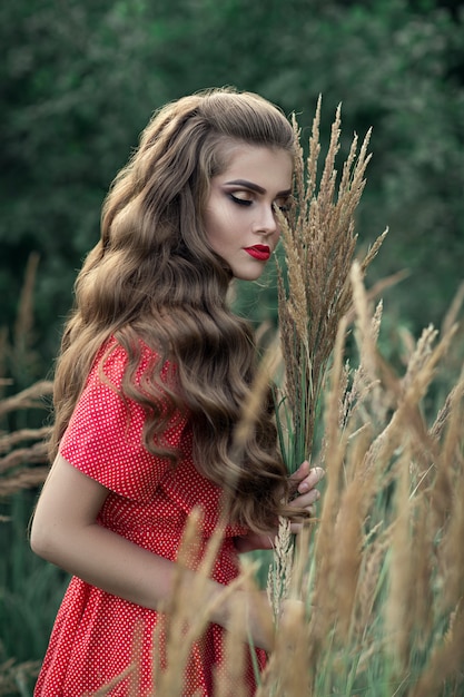 Bella giovane ragazza caucasica con lunghi capelli ondulati. Ritratto di una donna in un vestito rosso.