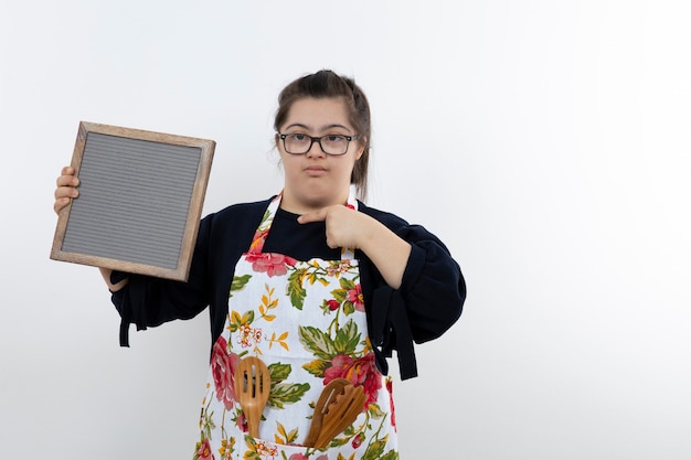 Bella giovane ragazza con sindrome di down in grembiule colorato che tiene cornice vuota.