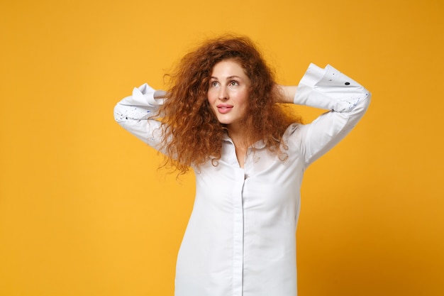 Bella giovane ragazza dai capelli rossi in camicia bianca casual in posa isolata sul muro giallo arancione yellow