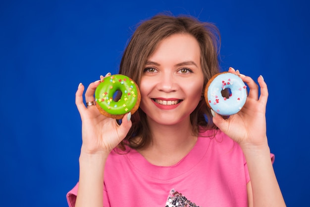 Bella giovane ragazza divertente con le ciambelle sul blu.