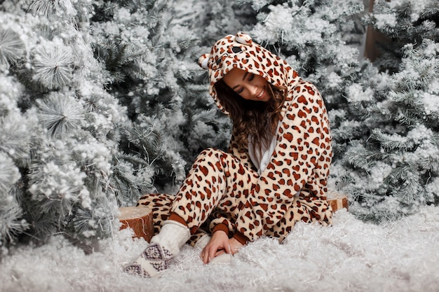 Bella giovane ragazza felice in pigiama orso divertente seduto vicino all'albero di Natale con la neve