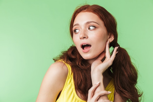 bella giovane ragazza rossa scioccata in posa isolata su sfondo verde muro.