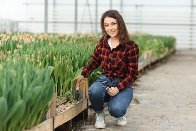 Bella giovane ragazza sorridente con tablet, lavoratore con fiori in serra.