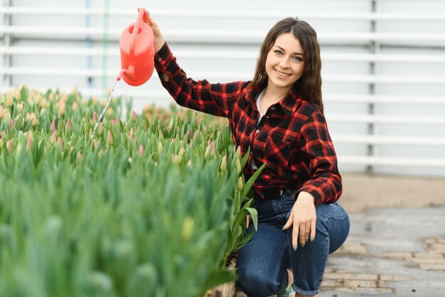 Bella giovane ragazza sorridente, lavoratore con fiori in serra.