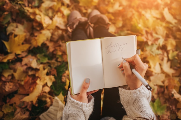 Bella giovane seduta castana sulle foglie di autunno cadute in un parco