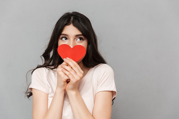 Bella giovane signora che copre il viso con il cuore