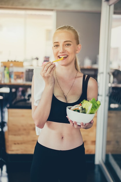 Bella giovane signora con insalata in palestra. Le donne sportive si esercitano con cibo sano. Salute mentale e benessere.