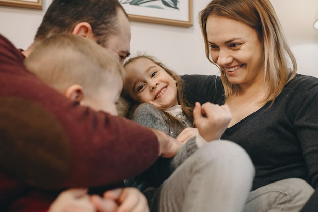 Bella grande famiglia che abbraccia e si diverte sul divano di casa loro mentre la bambina sorride.