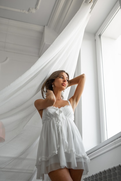 bella immagine gentile della sposa in una vestaglia bianca con il trucco vicino alla finestra