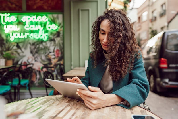 Bella imprenditrice riccia utilizzando la tavoletta digitale all'aperto nella caffetteria