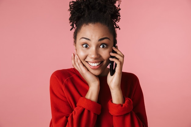 bella incredibile felice eccitata giovane donna africana in posa isolata sul muro rosa parlando al telefono cellulare.