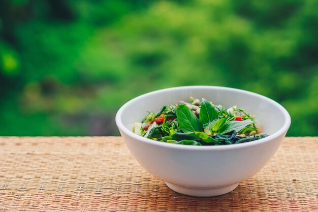 Bella insalata vegana cruda da foglie verdi mescolare le verdure in un piatto bianco Ricetta di cucina Pomodoro misto carota cavolfiore tagliato prezzemolo coriandolo aneto verde cetriolo basilico semi di zucca alghe