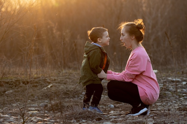 Bella madre che gioca con suo figlio in natura contro il tramonto. Festa della mamma concetto.