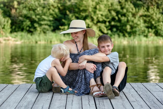 Bella madre con due figli piccoli si sta abbracciando sul molo sulla riva del fiume