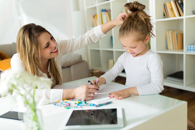 Bella madre con la figlia che disegna con i pastelli a casa.