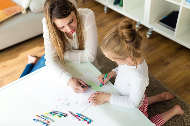 Bella madre con la figlia che disegna con i pastelli a casa.