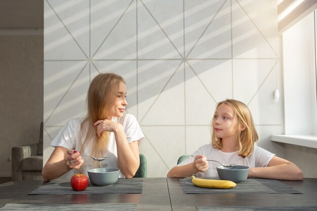 bella madre con la figlia in cucina a casa al tavolo mangiando porridge