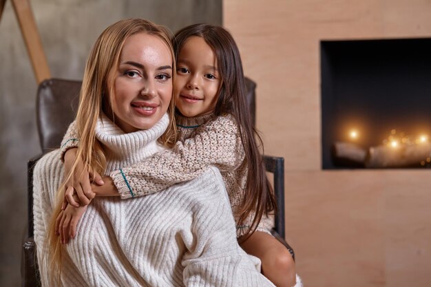 Bella madre donna in maglione bianco abbraccia la sua piccola figlia allegro umore giocoso e amore insi...