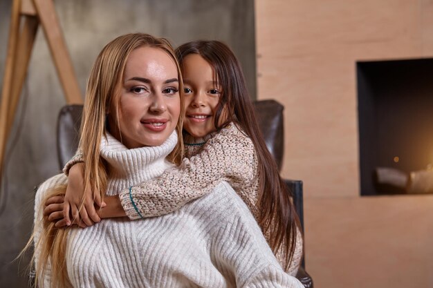 Bella madre donna in maglione bianco abbraccia la sua piccola figlia allegro umore giocoso e amore insi...