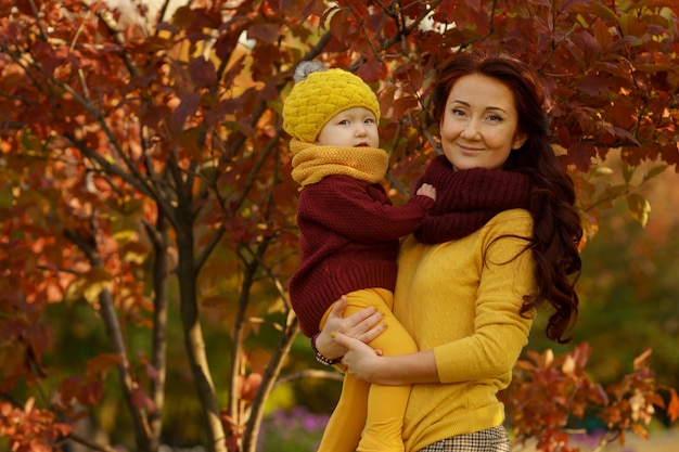 Bella madre e figlia vestite di bordeaux e giallo in scala di colori in posa guardando la telecamera nel soleggiato parco autunnale