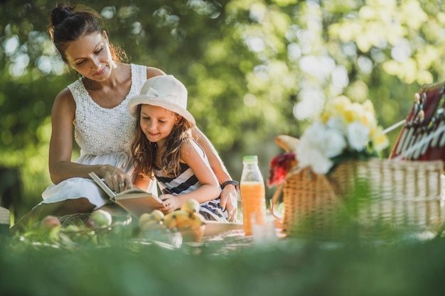 Bella madre e sua figlia carina che leggono un libro nel parco e si godono una giornata di picnic.