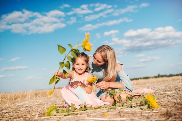 Bella madre premurosa si siede sul campo con la sua piccola bellissima figlia