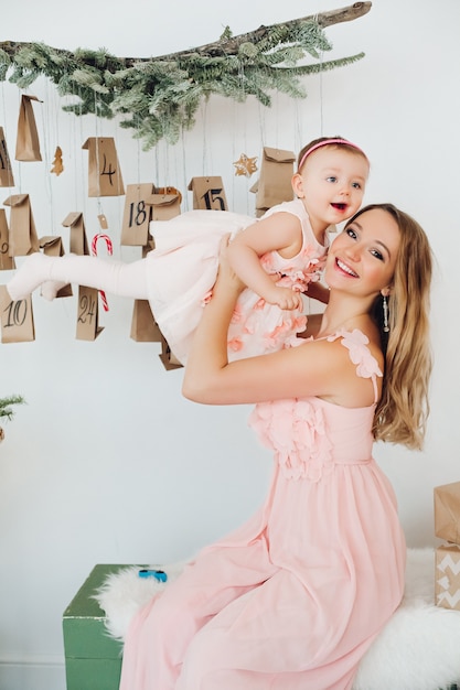 Bella mamma con figlia piccola in abiti rosa giocando vicino a decorazioni natalizie.