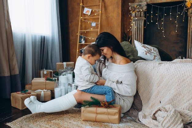 Bella mamma dai capelli castani e figlio adorabile del ragazzo che si siedono sul pavimento che abbracciano e che giocano