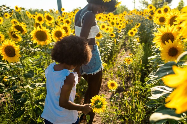 Bella mamma e figlia afroamericane che giocano e si divertono in un campo di girasoli