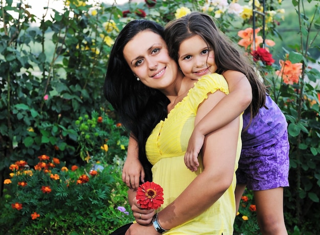 bella mamma e figlia all'aperto in giardino insieme al fiore si divertono e si abbracciano