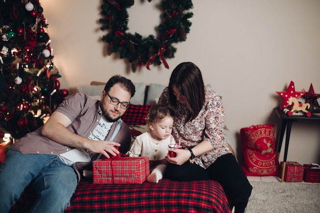 Bella mamma, papà e il loro bambino disimballano i regali di Natale