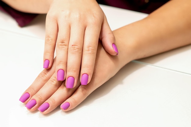 Bella manicure con smalto rosa porpora sulle mani delle giovani donne caucasiche