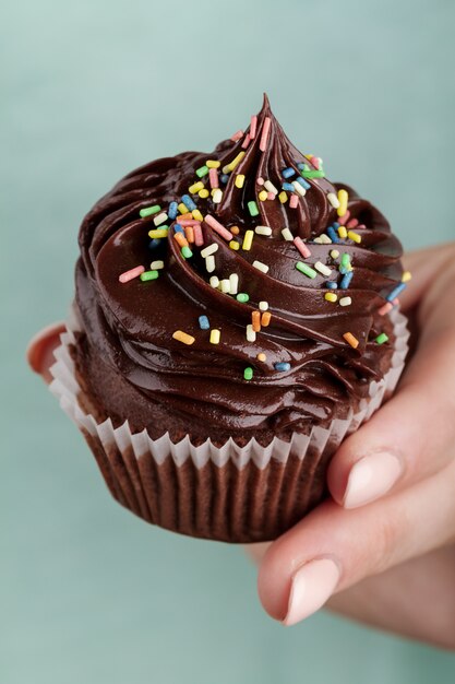 Bella mano femminile che tiene gustoso cupcake al cioccolato appetitoso. Sfondo blu. Avvicinamento.