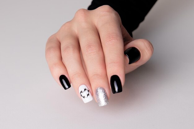 Bella mano femminile con unghie manicure nere design di cuori su sfondo bianco