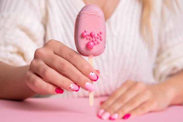 Bella mano femminile con unghie manicure rosa fiori design tenendo il gelato