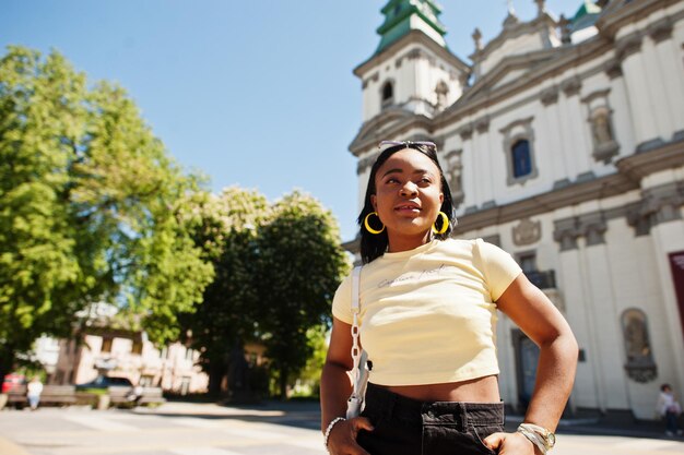 Bella moda giovane donna afroamericana in posa contro la cattedrale cattolica occhiali da sole giallo top Moda estate foto Colori vivaci Bella vista afro persone