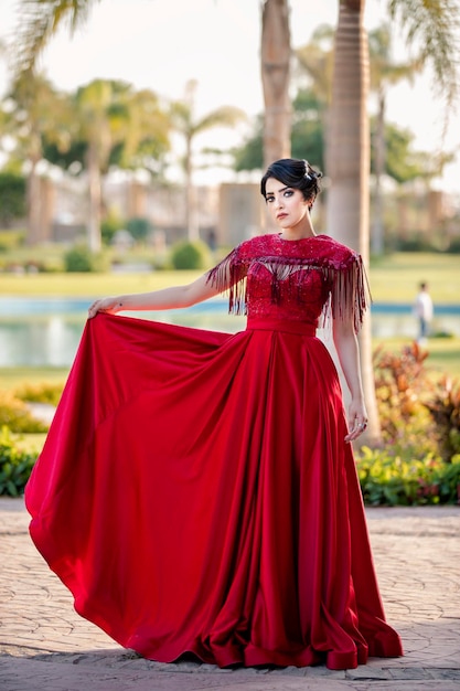 Bella modella in piedi che tiene la punta del suo lungo vestito rosso