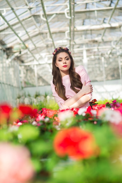 Bella modella vestita con un lungo abito rosa posa tra i tanti fiori della serra