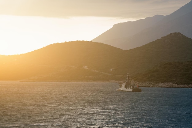 Bella nave marina che galleggia sull'acqua e sulla costa rocciosa all'alba o al tramonto