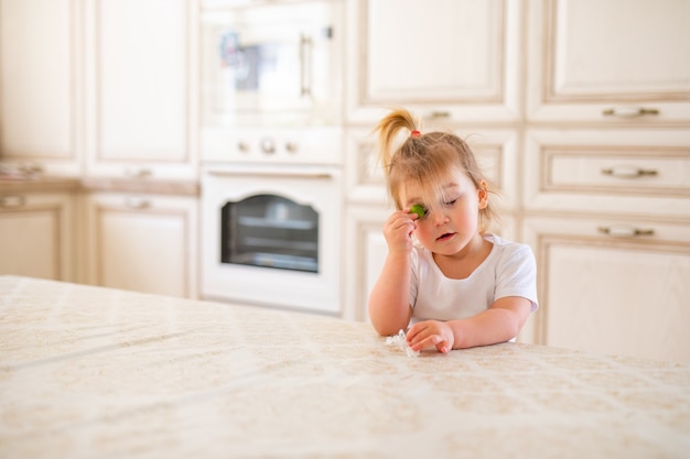 Bella neonata bionda che mangia prima colazione in cucina. Facce buffe