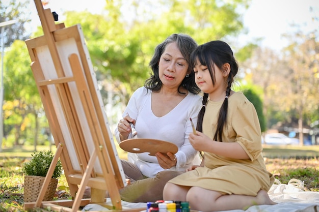 Bella nipotina asiatica che si concentra sulla pittura ad acquerello con sua nonna nel parco