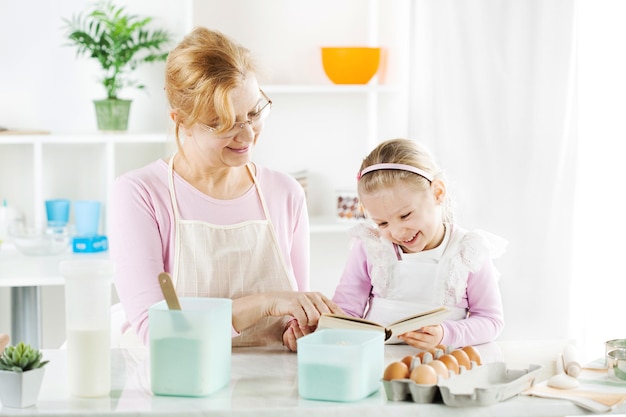 Bella nonna felice e nipote che leggono il libro di cucina in una cucina.