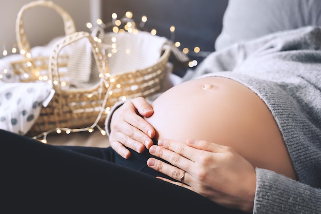 Bella pancia del primo piano della donna incinta in maglione lavorato a maglia alla luce delle ghirlande