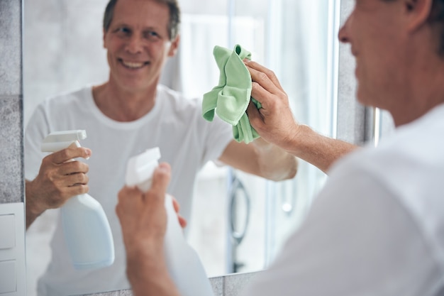 Bella persona di sesso maschile che mantiene il sorriso sul viso mentre fa le pulizie di casa